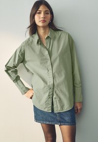 Chemise boutonnée vert clair à manches longues, associée à une mini-jupe en denim. Texture lisse, col classique, coupe décontractée.
