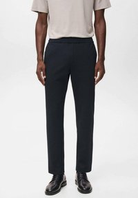 Marineblauwe tapershorts gemaakt van een gladde stof, met een platte voorkant en een elastische tailleband, gecombineerd met zwarte dresschoenen.