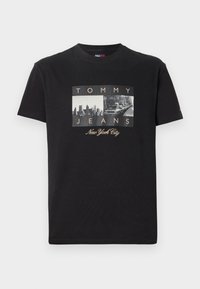 Must mustata T-särk, millel on graafika, kus on kaks vintage-stiilis fotot ja tekst "TOMMY JEANS" ning "New York City" kuldsete aktsentidega.