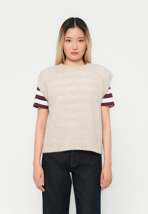 Beige strikkegenser med korte, polstrede skuldre og burgunderstriper på ermene, kombinert med mørkeblå denimbukser.