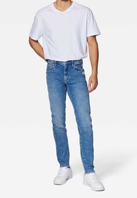 Herrarnas ljusblå denimjeans med smal passform, femfickorsdesign och lätta blekningsdetaljer, tillsammans med en vit bomull T-shirt och vita sneakers.