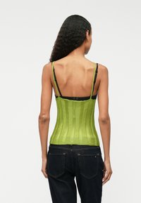 Zielony dzianinowy top w kształcie gorsetu z pionowym prążkowanym wzorem, cienkimi ramiączkami i dopasowanym krojem, w połączeniu z ciemnoniebieskimi dżinsami.