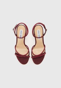 Burgundy high-heeled sandals with glittering straps and a smooth suede texture. Features two crisscrossing ankle straps and a buckle closure.