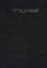 Schwarzer strukturierter Stoff mit erhabenem schwarzem Kolibri-Logo und dem eingeprägten Markennamen "hummel" nahe der oberen Mitte.