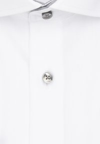 Gros plan sur le col et la patte de boutonnage d'une chemise blanche, avec deux boutons visibles, l'un gris et l'autre argenté.
