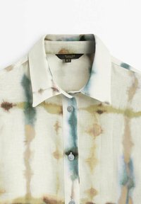 Linnepaita, jossa on vaalea beige tausta, jossa on abstrakteja sinisiä ja ruskeita kuvioita, terävä kaulus ja harmaat napit.