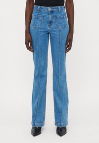 Blå denim flared jeans med høy midje, front- og baklommer, kontrasterende hvite sømmer, og en glatt tekstur.