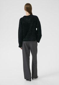 Czarny puszysty sweter z długimi rękawami, w komplecie z szarymi spodniami o szerokich nogawkach. Materiał ma miękką fakturę i lekko błyszczące wykończenie.