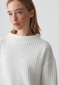 Weißer gerippter Pullover mit einem hohen, runden Ausschnitt. Hat einen strukturierten Stoff und lockere Ärmel, die ein weiches, minimalistisches Design zur Geltung bringen.