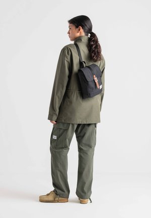 Olive green jacket and cargo pants, black backpack with a brown leather strap, textured fabric, and a casual design.