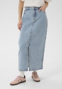 Svetlo modra denim maxi krila s sprednjim razporkom, visokim pasom in zankami za pas, kombinirana z rožnatimi športnimi copati in belimi nogavicami.
