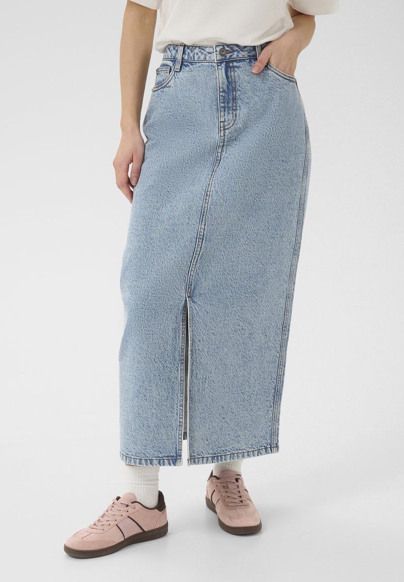 Svetlo modra denim maxi krila s sprednjim razporkom, visokim pasom in zankami za pas, kombinirana z rožnatimi športnimi copati in belimi nogavicami.