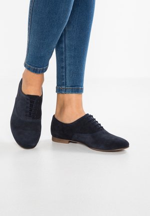 Marineblaue Wildleder-Schnürschuhe mit runder Zehenpartie und flacher, hellbrauner Sohle. Sichtbare Textur und Steppdetails am Obermaterial.