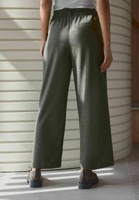 Pantalons large en vert olive avec une taille élastique et deux poches arrière. Le tissu a une texture douce et un léger éclat.