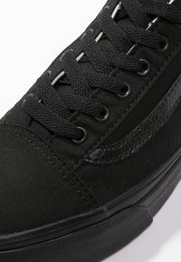 Sneaker nera con tomaia in tela, dettagli in pelle texture, lacci rotondi e suola in gomma. Presenta cuciture sottili e occhielli.