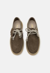 Zapatos de ante marrón con puntera redondeada, que cuentan con una entresuela texturada y cordones trenzados grises con detalles de borlas. Forro interior suave.