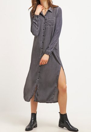 Szara sukienka koszulowa z długim rękawem, zapinana na guziki z przodu, z rozcięciami po bokach i kieszenią na piersi, wykonana z miękkiego, teksturowanego materiału.