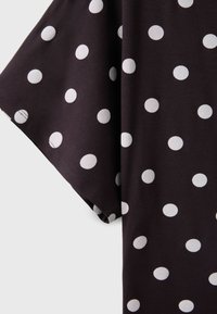 Black fabric with white polka dots, showing a close-up of a short sleeve garment with visible stitching on the hem.