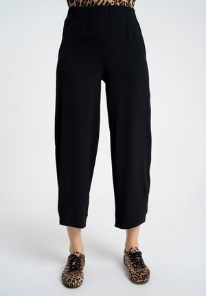 Czarne szerokie spodnie o długości do połowy łydki, noszone przez osobę stojącą w butach w panterkę i częściowo widocznej bluzce w panterkę.