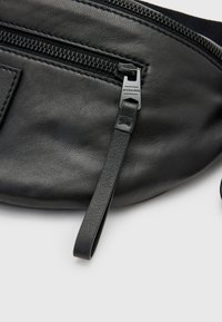 Zwarte leren heuptas met een gestructureerd oppervlak, sluiting met een bovenste rits en een kleine merkrits. Voorzien van een platte band voor een veilige draagwijze.