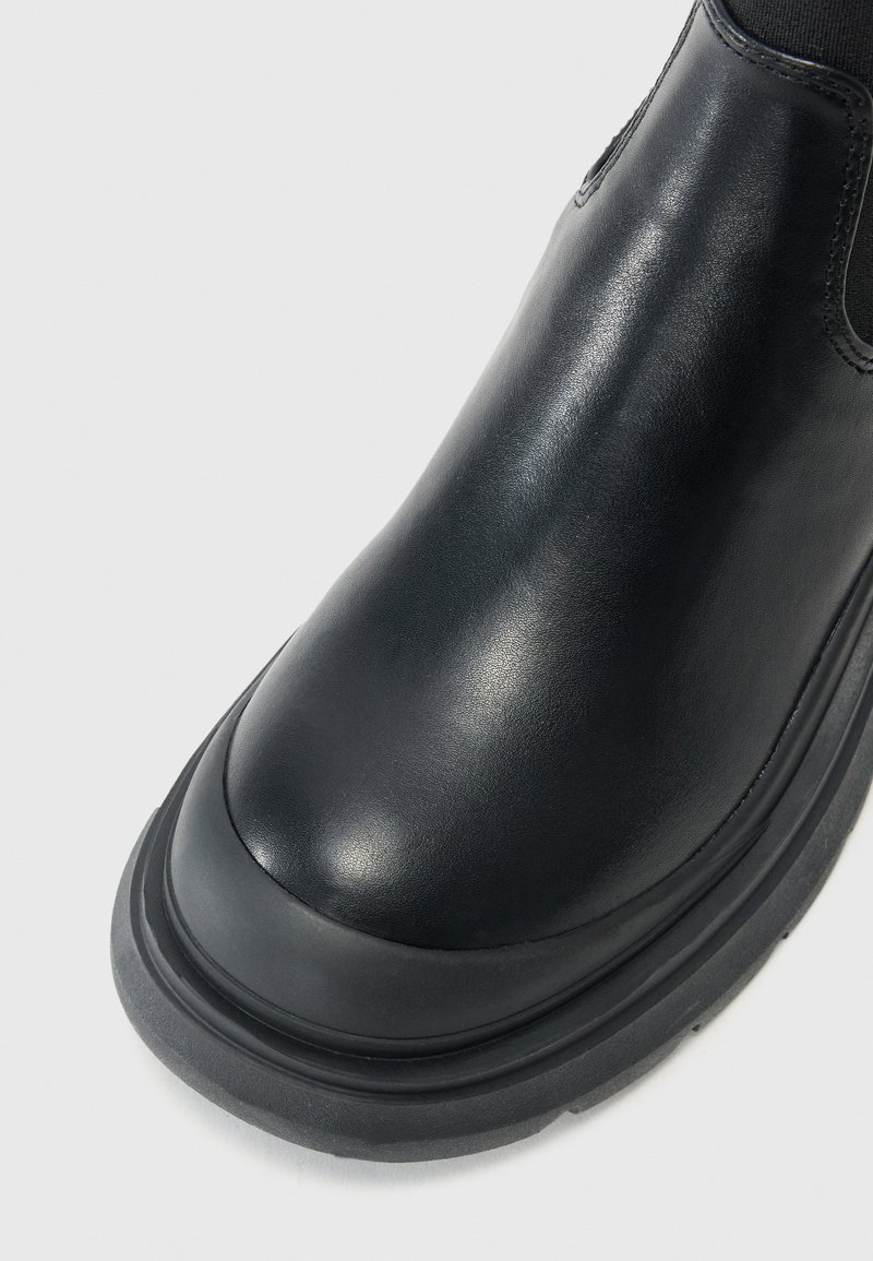 Bottines en cuir noir avec une texture lisse, bout rond et semelle en caoutchouc épaisse. Dotées de panneaux latéraux élastiques pour un enfilage facile.