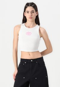 Bela rebrasta kratka majica z okroglim izrezom in roza vezenim logotipom na prsih, združena z visokim pasom črnih hlač s srebrnimi poudarki.