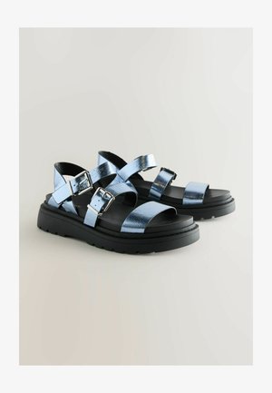 Plave metalik sandale s remenčićima i podesivim kopčama, crna debela potplata, otvoreni dizajn prstiju, glatka tekstura i suvremeni stil.
