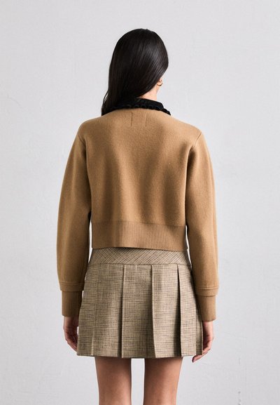 Rudas megztinis su trumpu dizainu ir raukšlėta apačia, derinamas su languota klostuota sijoną, kuriame yra tinklinis raštas ir tekstūruotas audinys.