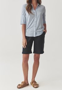 Light blue, button-up shirt with rolled sleeves, paired with navy shorts. Worn with brown sandals. Soft fabric, casual fit.