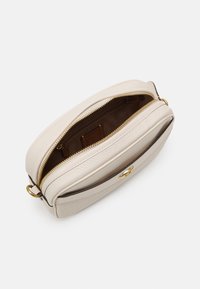 Krémová kožená taška s texturovaným povrchem, vybavená zlatým zipovým uzávěrem a hnědým interiérem. Zdobení zahrnuje zlatý kovový detail.