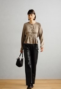 Beige satin blouse with a gathered waist and buttons, paired with black leather straight-leg trousers. Model holds a small black bag.