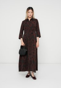 Robe longue marron à motifs floraux, avec un devant à boutons, manches trois quarts ; accompagnée d'un sac à main noir et de ballerines bordeaux brillantes.