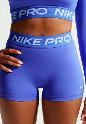 Atleta vistiendo pantalones cortos de compresión Nike Pro púrpura y camiseta a juego, con la marca Nike visible en la cintura y la parte inferior de la pierna izquierda.