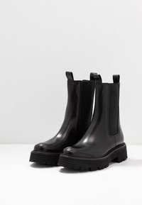 Schwarze Leder Chelsea-Boots mit elastischen Seitenpaneelen und Handgriff. Dicke Gummisohle mit strukturiertem Profil für guten Halt. Glatte Oberfläche.