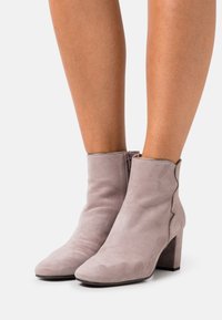 Botas de tobillo de ante gris con cremallera lateral, tacón cuadrado, puntera afilada y un detalle ondulado a lo largo del borde superior. Textura suave en toda la superficie.