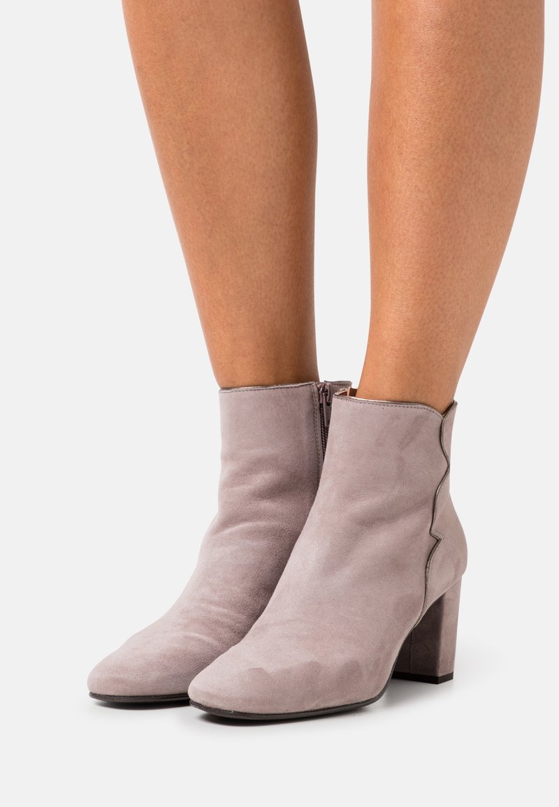 Botas de tobillo de ante gris con cremallera lateral, tacón cuadrado, puntera afilada y un detalle ondulado a lo largo del borde superior. Textura suave en toda la superficie.