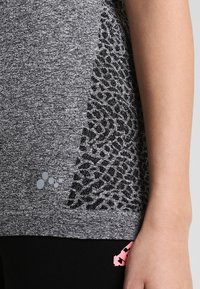 Top sportivo grigio heather con un pannello laterale caratterizzato da un motivo testurizzato nero, impreziosito da un piccolo logo grigio vicino all'orlo.