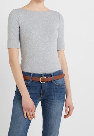 Mujer vestida con una camiseta ajustada gris claro con mangas hasta el codo, vaqueros azules y un cinturón de cuero marrón con hebilla dorada.