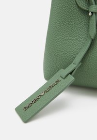 Zielona skórzana torebka o teksturowanym wykończeniu z dekoracyjną zawieszką z napisem "Emporio Armani" w metalicznej literze.