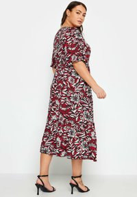 Blumen-Midi-Kleid mit einem roten, schwarzen und weißen botanischen Muster, kurzen Ärmeln und einem ausgestellten Saum. Getragen mit schwarzen Riemchenschuhen.