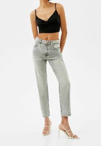 Černý kr short top, světlé šedé džíny s vysokým pasem a béžové sandály na vysokém podpatku se zavazováním; ležérní outfit s uvolněným střihem a světlou texturou.