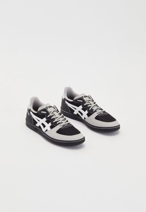 Par lavtop sorte og grå sneakers med hvide striber og snørebånd mod en ensfarvet lys baggrund.