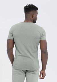 Camiseta de manga corta en color verde menta fabricada con un tejido suave y texturizado. Presenta un cuello redondo y un corte ajustado, con una etiqueta de marca sutil cerca del cuello.