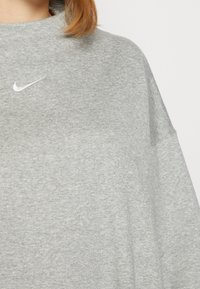 Grå, oversized sweatshirt gjord av mjukt, texturerat tyg. Har en vit Nike-logotyp på bröstet och vida ärmar för en avslappnad passform.