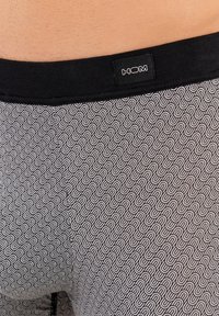 Mutande da uomo con motivo, caratterizzate da un elastico in vita nero con logo. Il tessuto presenta un design a onde ripetitive in grigio e bianco.