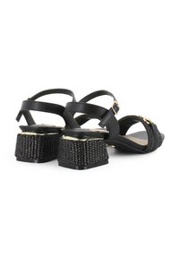 Sandalias negras con un tacón tejido texturizado, hebillas ajustables y una parte superior de cuero suave. Diseño de punta abierta con acentos dorados.