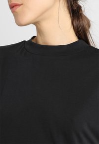 Svart kortärmad topp med rund halsringning, tillverkad av slät tyg, med en ren design utan mönster eller detaljer.