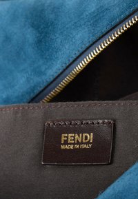 Gros plan d'un sac en daim bleu avec une fermeture éclair dorée et une étiquette en cuir marron embossée de la mention FENDI Made in Italy à l'intérieur.