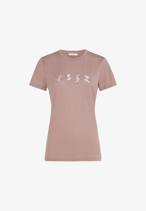 Ljusrosa t-shirt med kort ärm tillverkad av mjukt tyg, med vita tryck av skidåkning över bröstet. Klassisk design med rund halsringning.