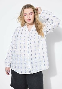 Vit skjorta med blå diamantmönster, lång ärmar med elastiska manschetter, och en avslappnad passform. Kombination med mörka shorts.